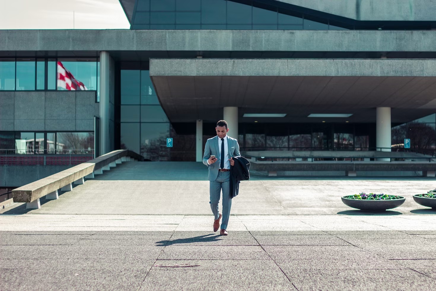 A businessman walking on an empty compound holding his phone.